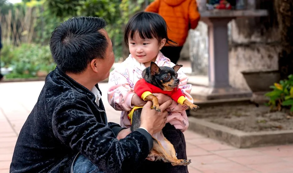 A heartwarming moment of a father holding his daughter and their cute pet dog outdoors.