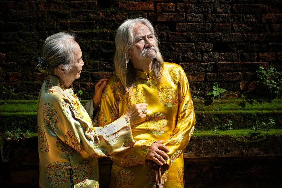 Elderly Vietnamese couple in traditional attire outdoors, showcasing cultural heritage.