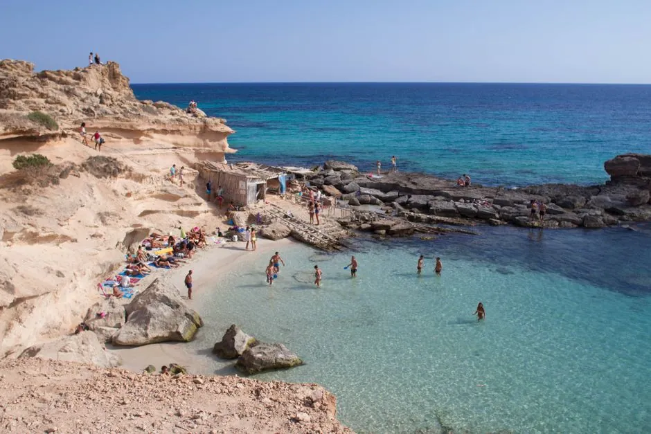Stunning coastline photo capturing beachgoers at a rocky cove in Illes Balears, Spain.