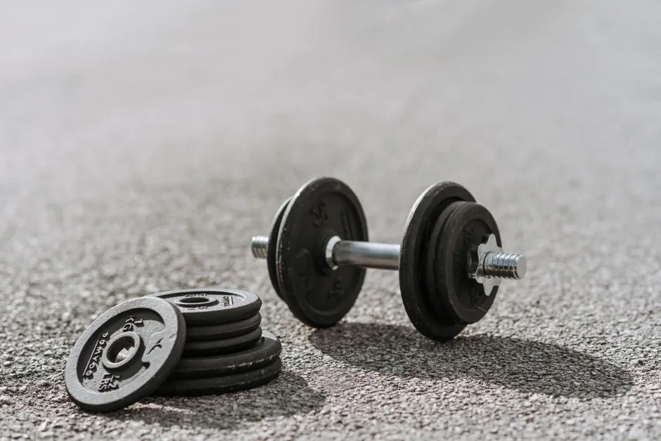 Modern adjustable dumbbell with stainless steel bar and cast iron plates on asphalt road with shadows