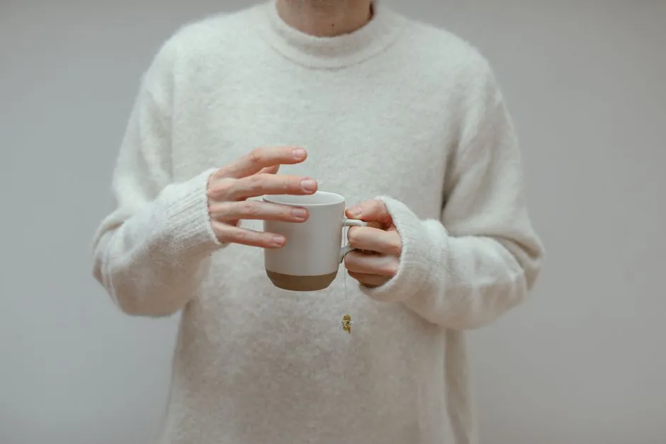 Close-up of a person holding a ceramic mug with tea in a cozy knitted sweater.