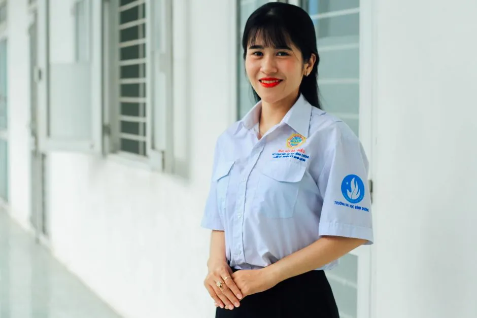 Confident Asian woman smiling in a professional setting, wearing a uniform indoors.