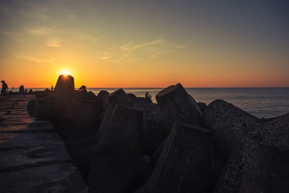 Serene sunset view over Haiphong sea barrier, featuring silhouetted fishermen and calming ocean waves.