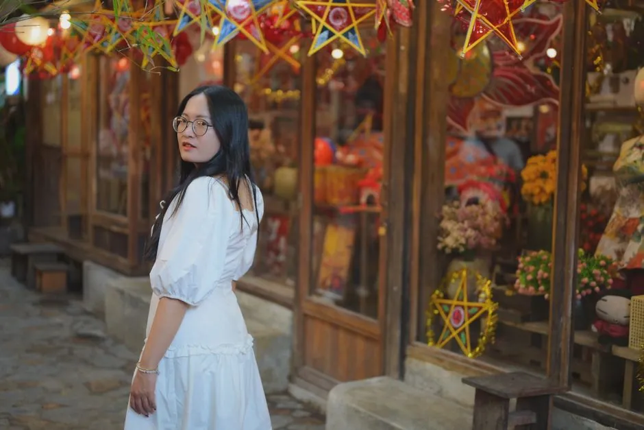 Young woman in a white dress with glasses at a vibrant outdoor market adorned with colorful star decorations.