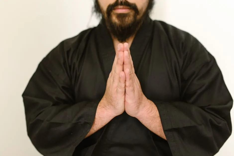 A focused martial artist in a black gi with hands in prayer position, indoors.