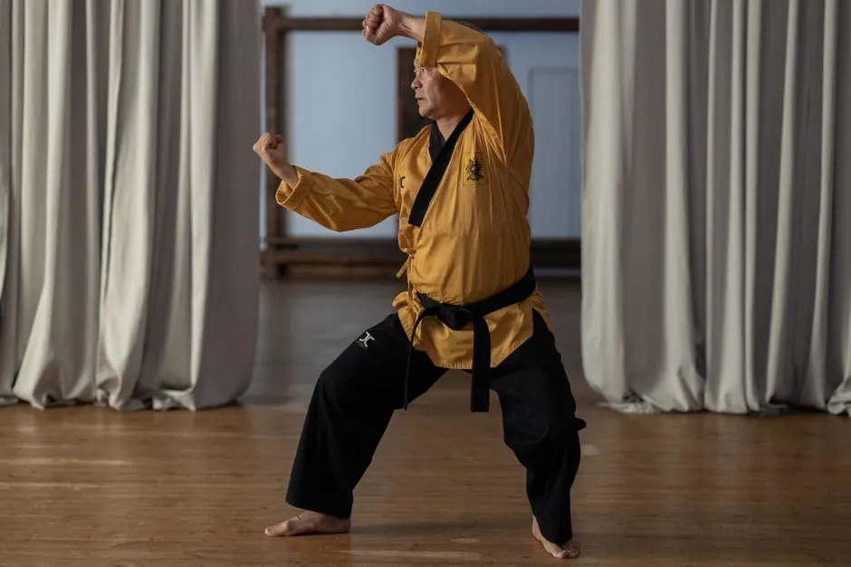 A senior man practicing martial arts indoors, showcasing traditional techniques and poses.