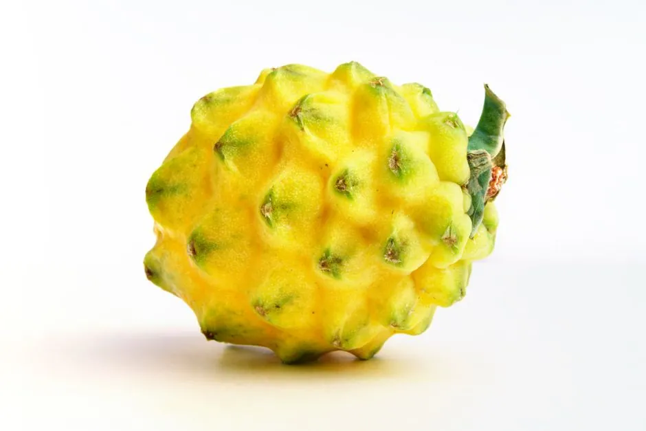 Close-up of a vibrant yellow dragon fruit isolated on a white backdrop, showcasing its exotic texture.